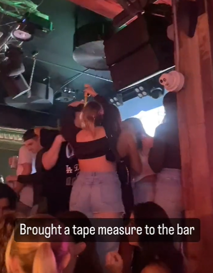 woman uses tape to measure height of men at bar